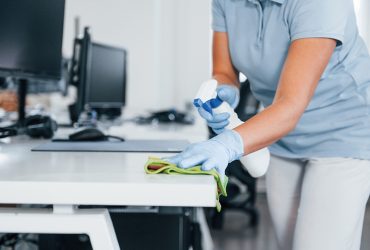 Close up view of woman in protective gloves that cleaning tables in the office.